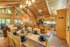 A wooden cabin interior with a dining area, kitchen, and a large chandelier.