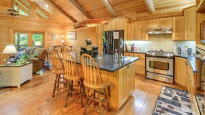 Une cuisine spacieuse avec des meubles en bois, un grand îlot central doté de tabourets, un réfrigérateur, une cuisinière et un coin repas avec un canapé et une table.