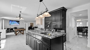 Una cucina moderna con mobili scuri, un piano di lavoro in marmo e illuminazione a sospensione.