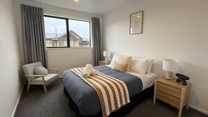 Quarto de hotel com cama, cadeira, mesa de cabeceira, luminária e janela com cortinas.