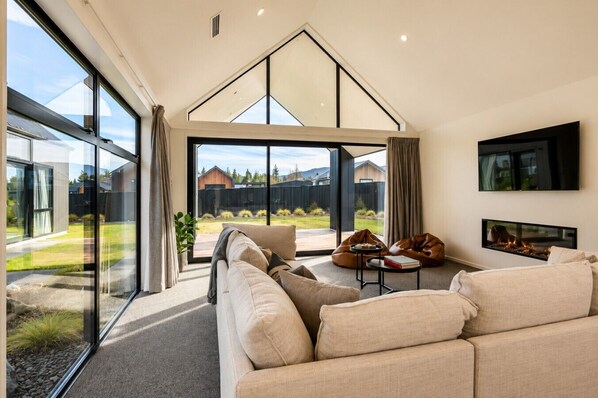 A modern living room with a large window, a fireplace, and a flat-screen TV.