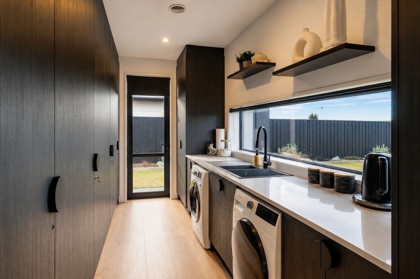 A modern kitchen with a built-in washer and dryer, a large window, and a view of the backyard.