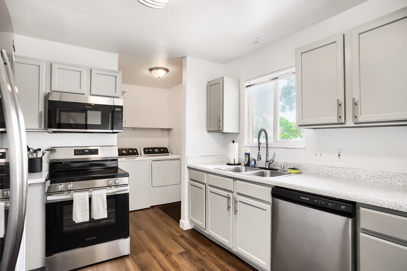 A modern kitchen with stainless steel appliances, white cabinetry, and a window providing natural light.