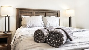 Ein ordentlich bezogenes Bett mit einer gestreiften Decke, zwei Nachttischlampen und einem Holzkopfende.