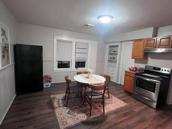 A compact kitchen with a dining table, chairs, a refrigerator, oven, and cabinets.