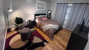 Une chambre à coucher comprenant un lit, une table de chevet, une lampe, une chaise, un pouf et un meuble pour la télévision.