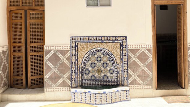 Interior tradicional com duas portas de madeira, parede com azulejos e uma pequena mesa.
