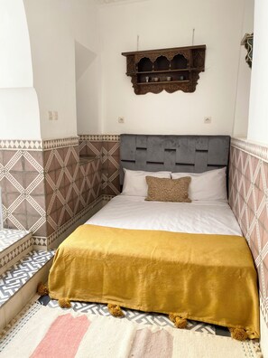 A bedroom with a bed, patterned walls, a decorative shelf, and a patterned rug. - A 4-bedroom Riad in the heart of the Marrakech Medina - perfect for groups! (Marrakesh)