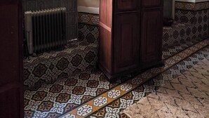 Quarto com ladrilhos estampados, radiador, armário e janela com vista para vegetação.