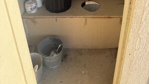 A small, enclosed bathroom with a toilet, a trash bin, and a bucket. - Lone Star Observatory: Off-Grid Big Bend Cabin Under the Darkest Skies (Alpine)