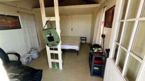 A small, single-room accommodation with a bed, a chair, a table with various items, and a ladder. - Lone Star Observatory: Off-Grid Big Bend Cabin Under the Darkest Skies (Alpine)