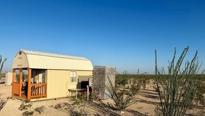 A small, single-story building with a porch and a window, surrounded by desert vegetation. - Lone Star Observatory: Off-Grid Big Bend Cabin Under the Darkest Skies (Alpine)