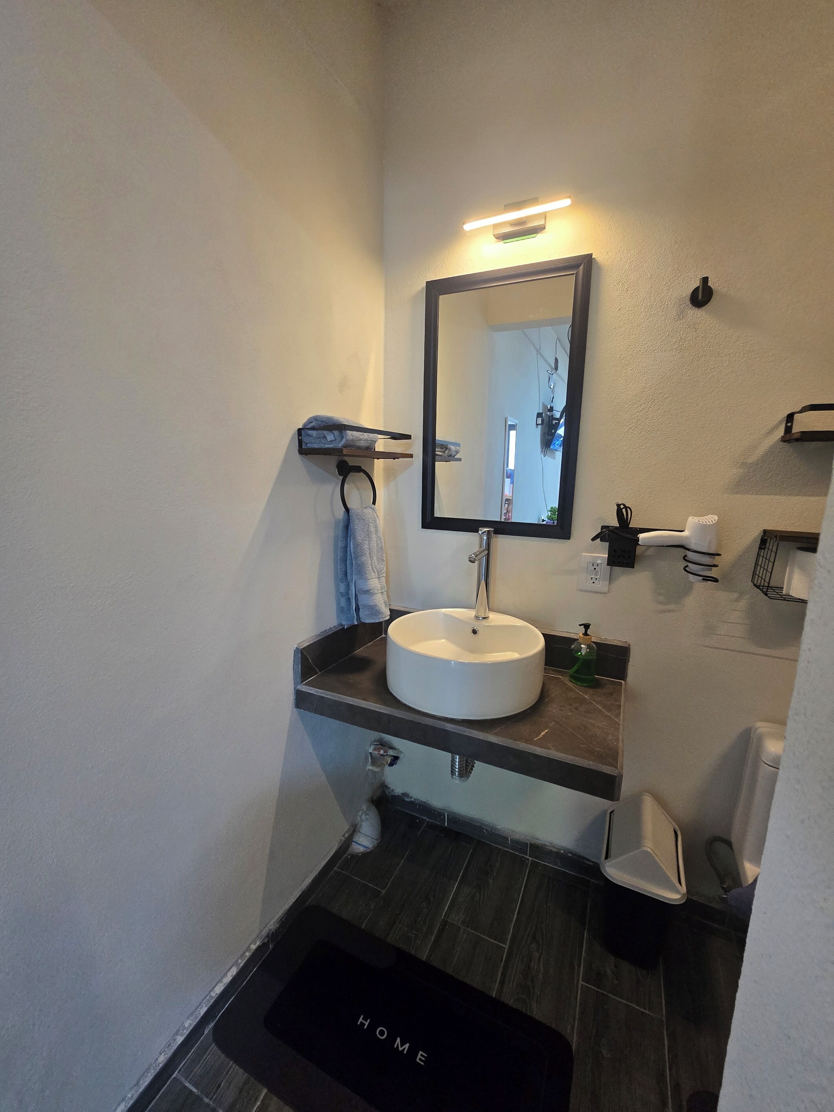 A bathroom with a white sink, a mirror, a towel rack, a soap dispenser, and a 'HOME' mat.