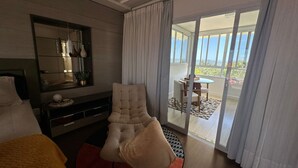 Et moderne hotelværelse med en stor seng, et siddeområde med stol og bord, et fjernsyn og en skydedør til en balkon.