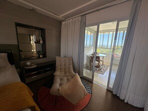 Ein modernes Hotelzimmer mit einem großen Bett, einer Sitzecke inklusive Sessel und Tisch, einem Fernseher und einer Glastür zum Balkon.