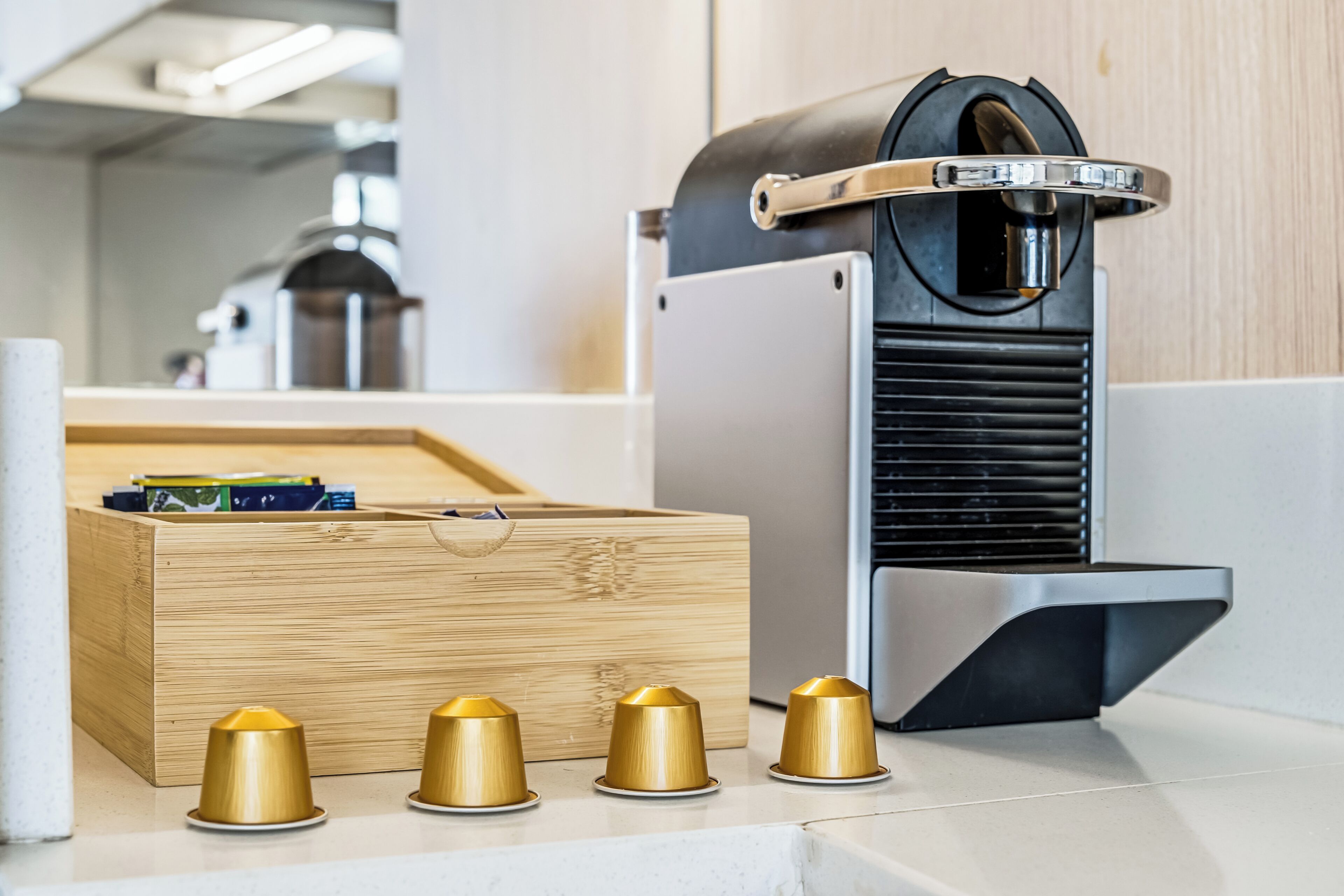 A coffee machine with a black and silver design, a wooden box with compartments, and three gold-colored cups on a countertop.