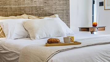 Un lit bien fait, avec un plateau contenant des articles pour le petit-déjeuner, un oreiller et une table de chevet sur laquelle se trouve une lampe.