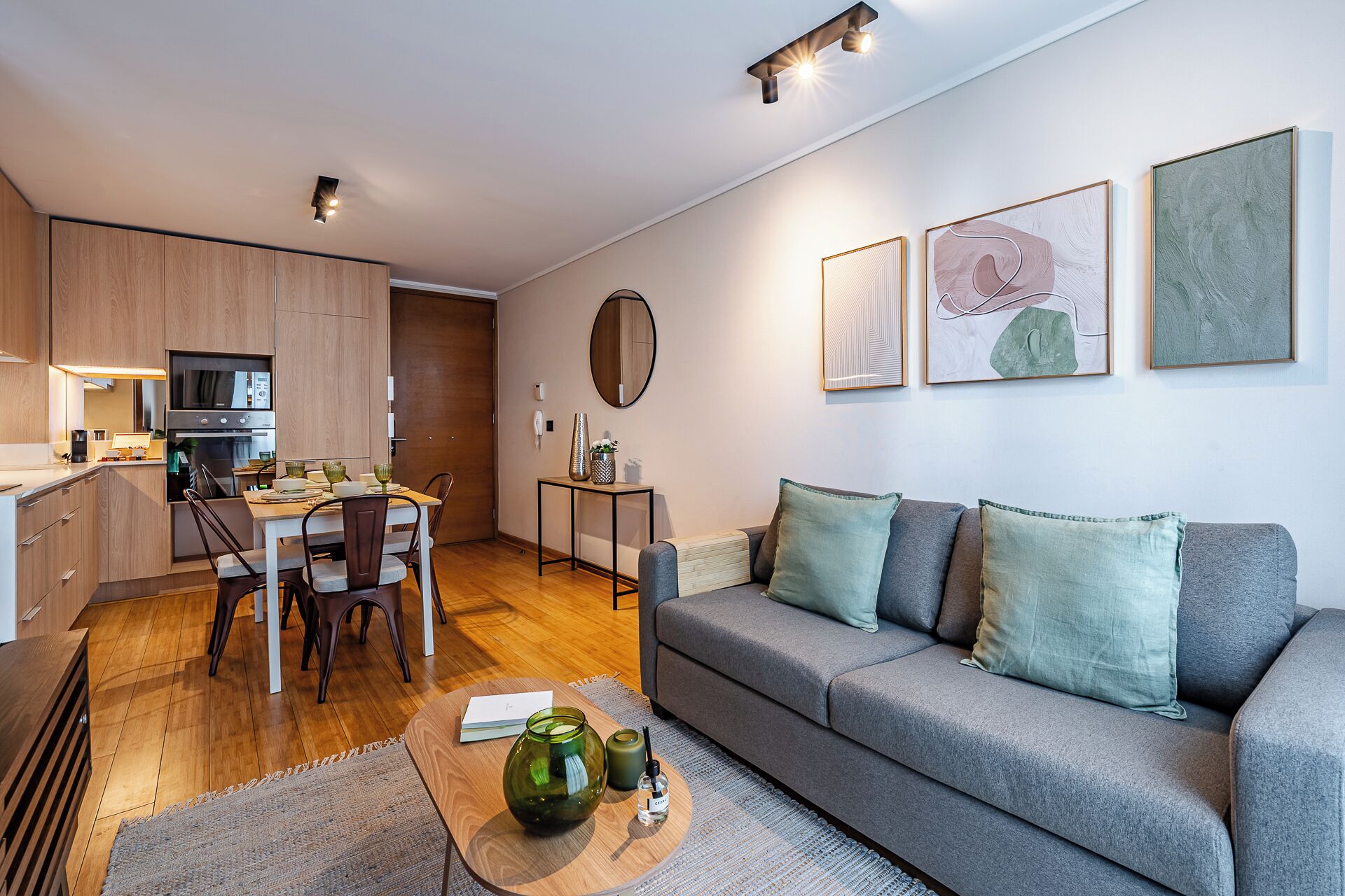 A modern living space with a kitchen, dining area, and a grey sofa with cushions.