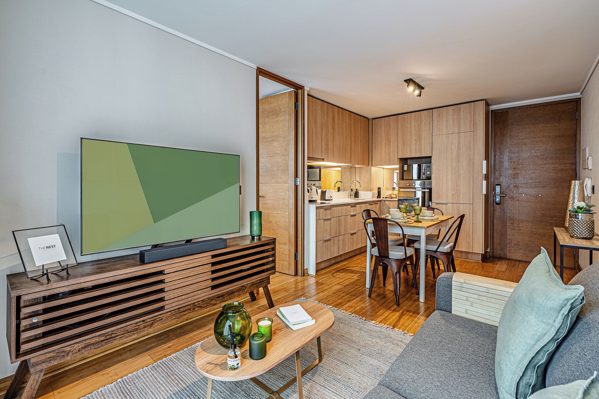 A modern living room with a flat-screen TV, wooden furniture, a dining area, and a kitchen.