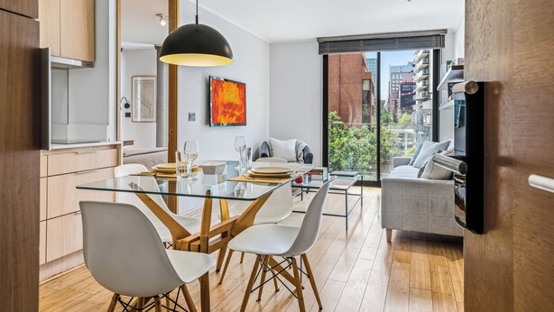 A modern kitchen with a glass dining table, white chairs, and a black pendant light. - Nest Collection El Golf (Las Condes)