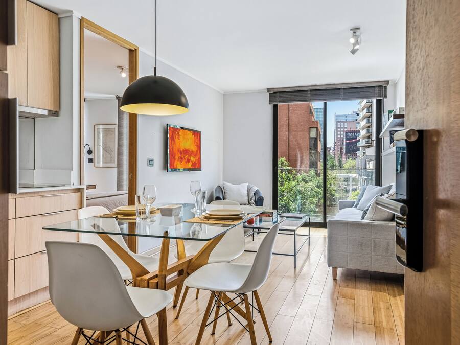 Una cocina moderna con una mesa de comedor de cristal, sillas blancas y una lámpara colgante negra.