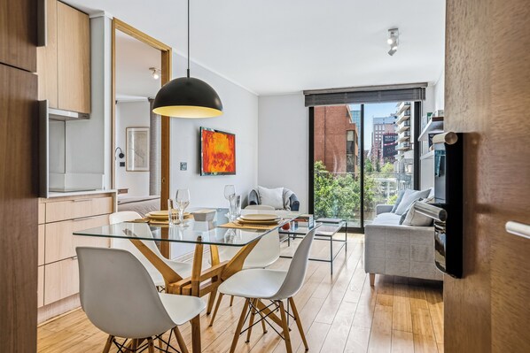 Una cocina moderna con una mesa de comedor de cristal, sillas blancas y una lámpara colgante negra.