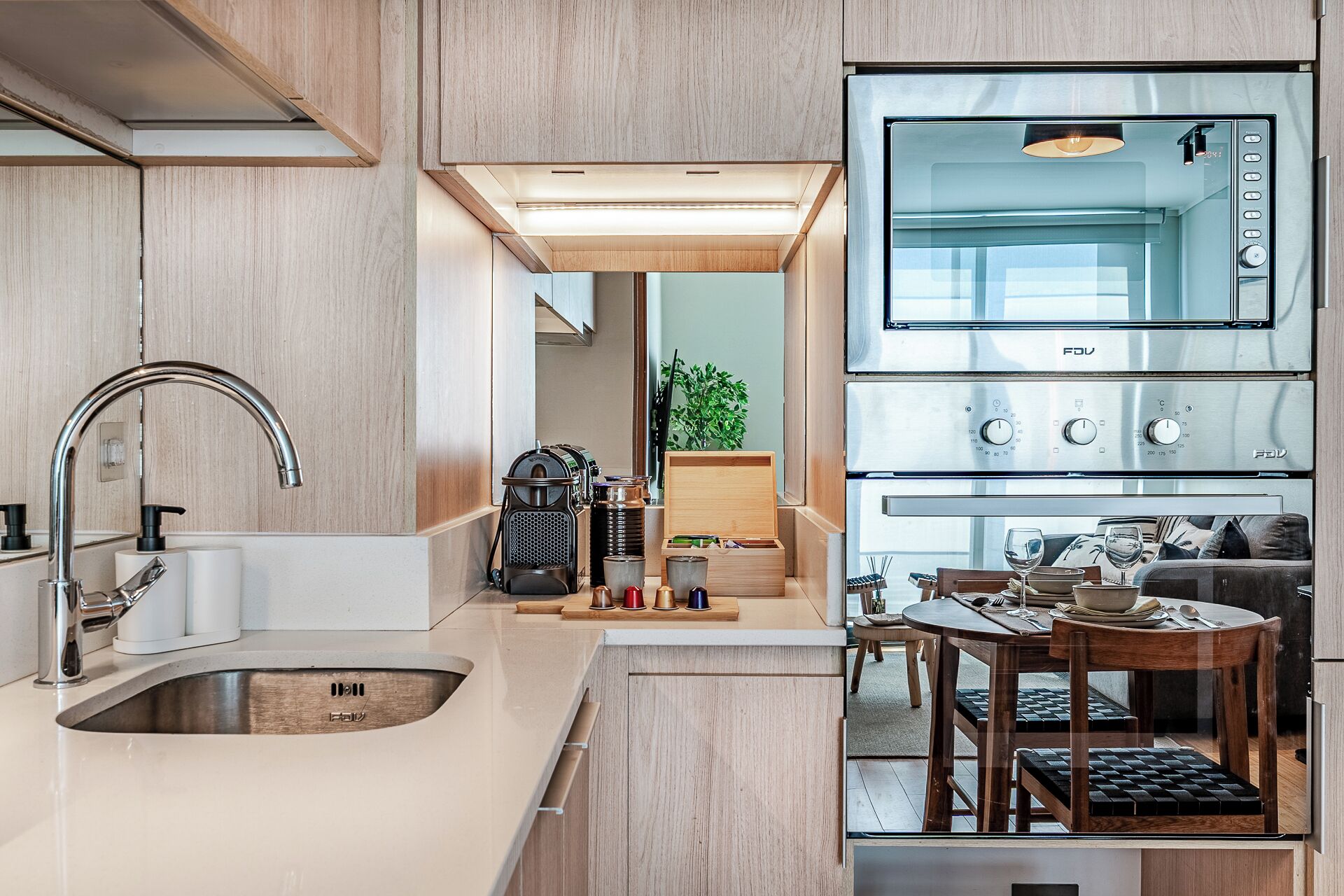 A modern kitchen with a built-in oven, a sink, and a dining area with a table and chairs.