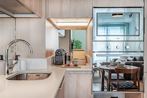 Una cocina moderna con horno empotrado, un lavamanos y una zona de comedor con mesa y sillas.