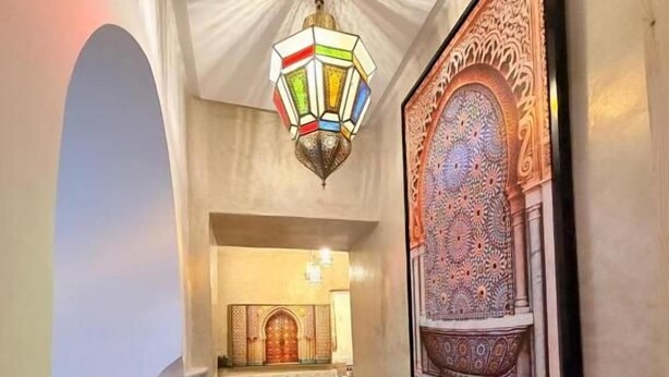 Un pasillo con intrincados trabajos en mosaico, un farol colgante y una pieza decorativa enmarcada en la pared.