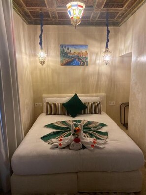 Ett hotellrum med en säng, en tavla, två vägglampor och en dekorativt arrangerad handduk.