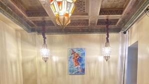 Una habitación de hotel con una cama, almohadones decorativos, un cuadro en la pared y una araña.
