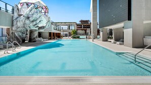 Une piscine agrémentée d’une grande sculpture en forme de main, des bâtiments modernes et un ciel dégagé.