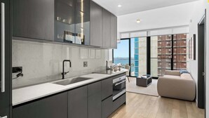 Une cuisine moderne dotée d’un grand îlot central, d’un four encastré et offrant une vue sur la ville grâce à de grandes fenêtres.