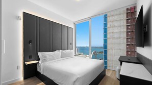 Une chambre moderne avec un grand lit, une table de chevet, une télévision et une vue sur la ville et l’eau.