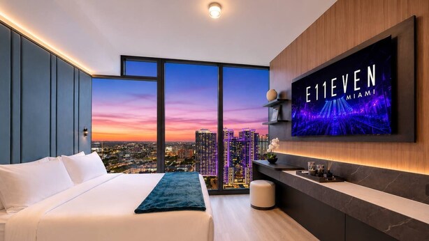A modern hotel room with a large bed, a TV mounted on the wall, and a city view. - Deluxe E11EVEN Suite with Elite Amenities (Miami)
