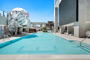 A swimming pool with a large hand sculpture, modern buildings, and a clear sky. - Deluxe E11EVEN Suite with Elite Amenities (Miami)
