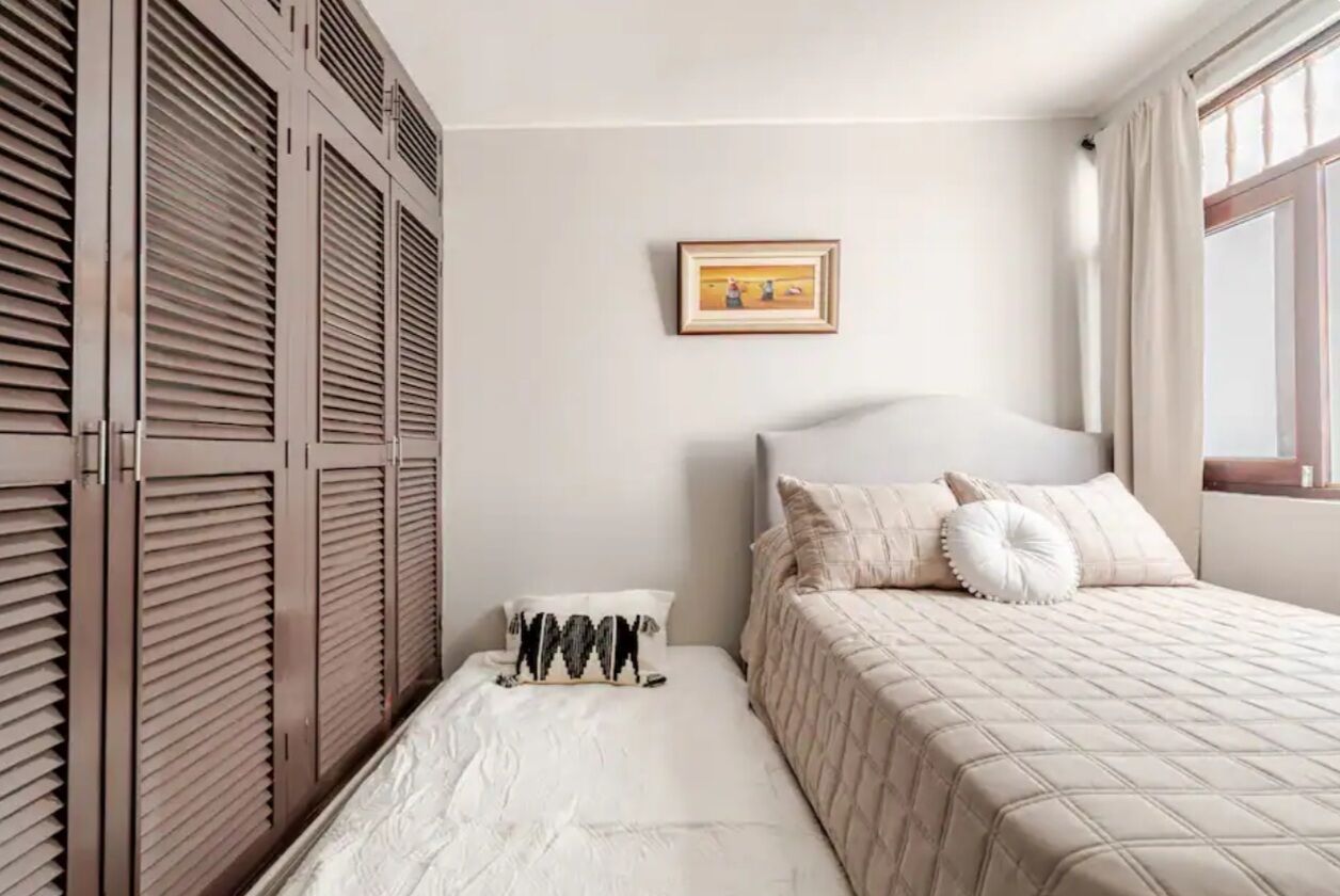 A bedroom with a bed, a bedside table, a wardrobe, and a painting on the wall.