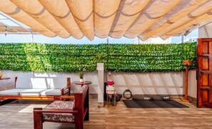 An outdoor seating area with a wooden table and chairs, a wall of green foliage, and a wooden door. - Spacious 5BR for Groups. Rooftop Terrace. Near Malecón & Airport (San Miguel)