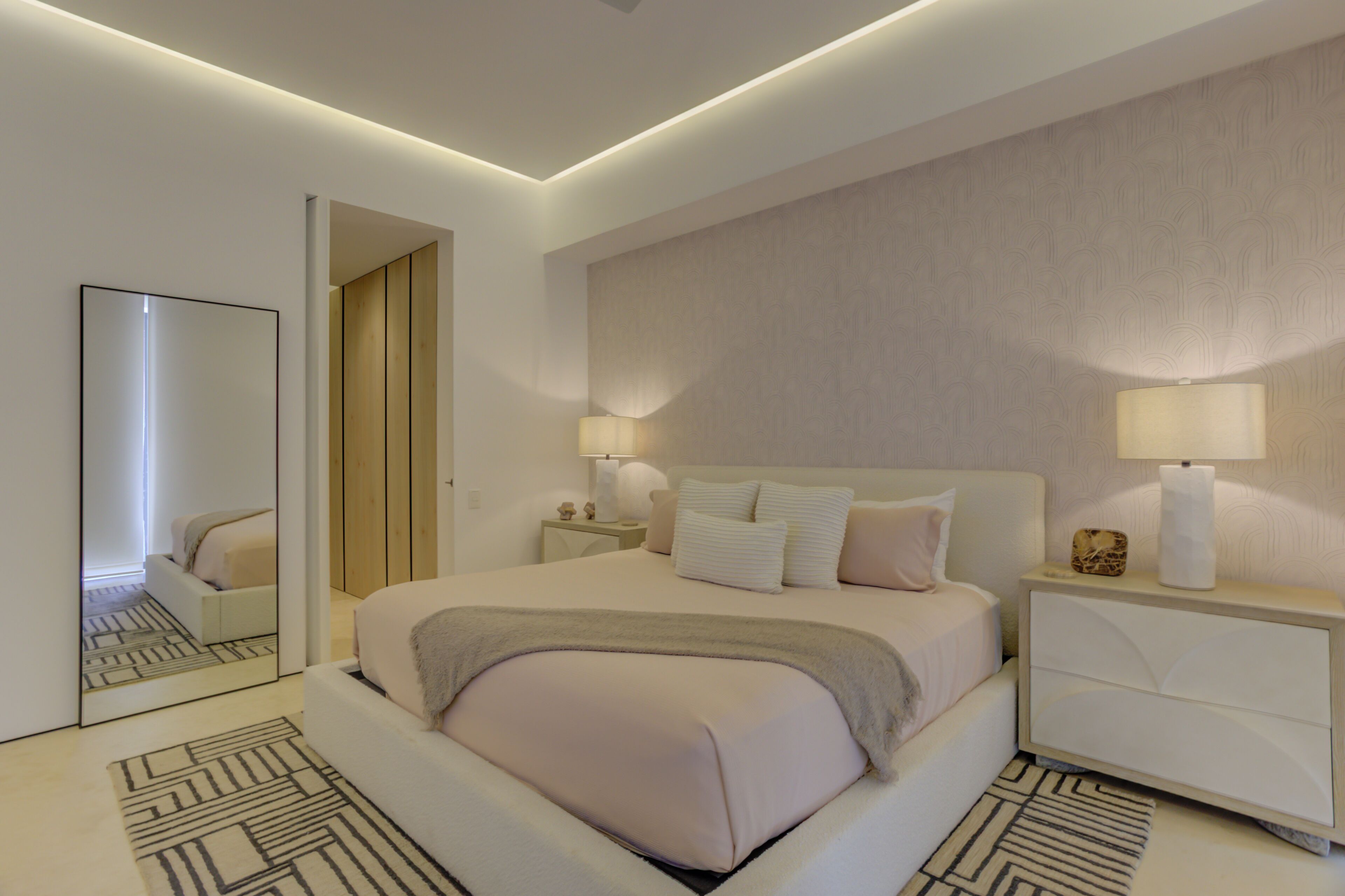 Una habitación de hotel moderna con una cama grande, lámparas de noche, una mesita de noche y un espejo.
