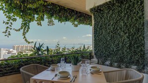 Une table à manger dressée avec des assiettes, des verres et des couverts, donnant sur un paysage urbain avec vue sur la mer.
