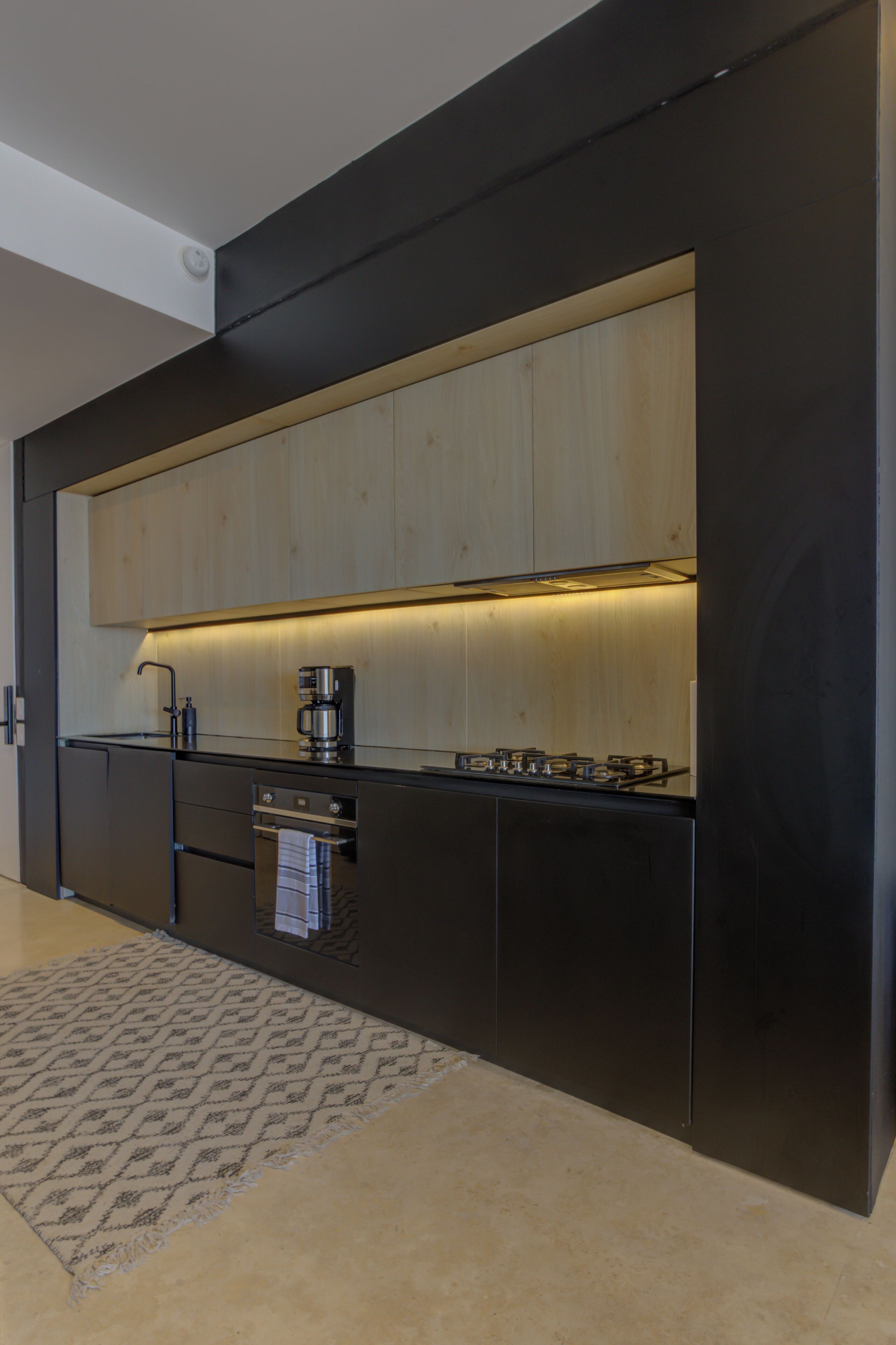 Una cocina moderna con armarios negros, encimera de madera, estufa a gas, cafetera y alfombra estampada.