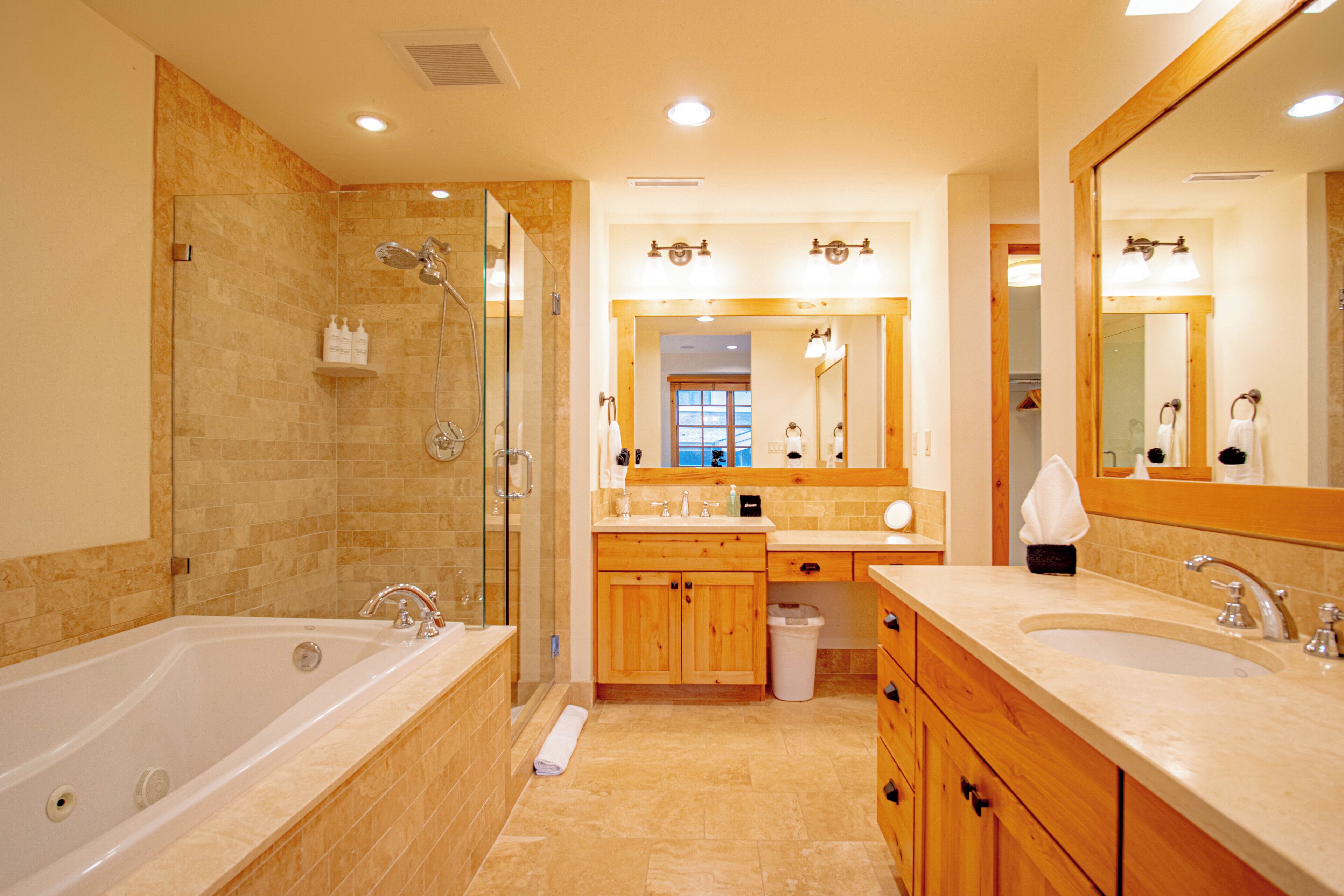 A modern bathroom with a large bathtub, a shower area, wooden cabinets, and a large mirror.