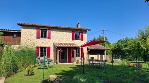 Una casa de piedra con contraventanas rojas, un patio con sillas y un jardín cercado.