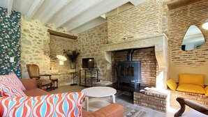 Ein gemütliches Wohnzimmer mit Steinwand, Kamin, Fernseher und einer Couch mit gemusterten Kissen.