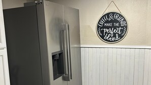 Een keuken met een roestvrijstalen koelkast, een zwarte prullenbak en een bord waarop staat: 'Coffee & Friends Make the Perfect Blend'.