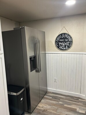 Una cocina con un refrigerador de acero inoxidable, un bote de basura negro y un letrero en la pared que dice 'Coffee & Friends Make the Perfect Blend'.