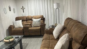 Een woonkamer met een bruine bank, een glazen salontafel en een lamp.