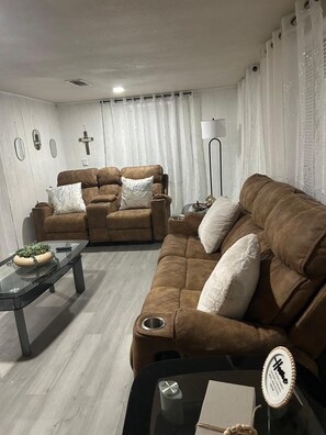 Una sala de estar con un sofá marrón, una mesa de centro de vidrio y una lámpara.