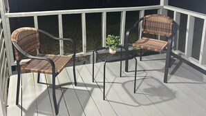 Een overdekt terras met twee rieten stoelen en een kleine tafel, omringd door witte hekken.