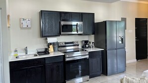 A modern kitchen with dark cabinetry, stainless steel appliances, and a tiled floor. - Spacious, cool, and tastefully decorated one bedroom with pull out sofa. (Kingston)